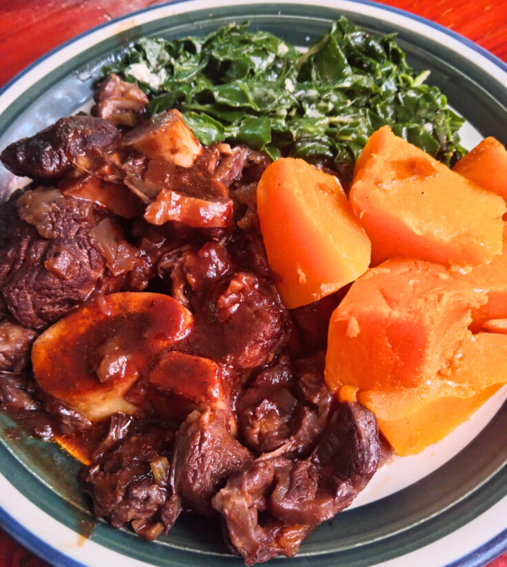 Braised beef shin with rich red wine jus, creamed spinach, and buttered pumpkin served on a white plate.