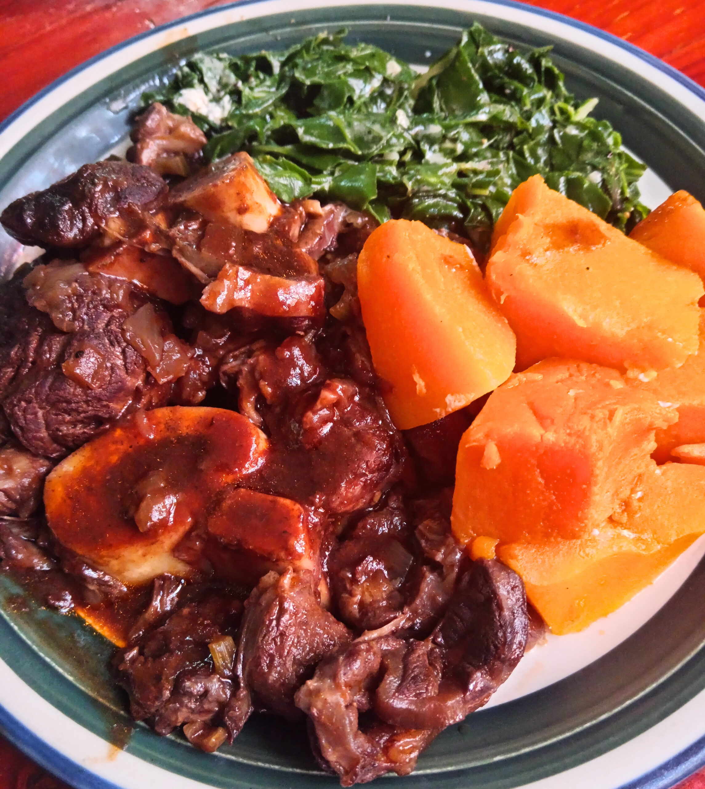 Braised beef shin with rich red wine jus, creamed spinach, and buttered pumpkin served on a white plate.