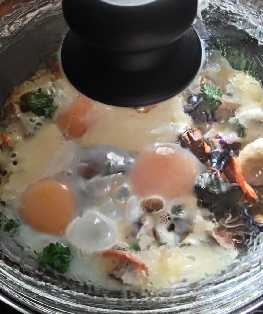 Eggs and mozzarella steaming under a glass lid in a frying pan