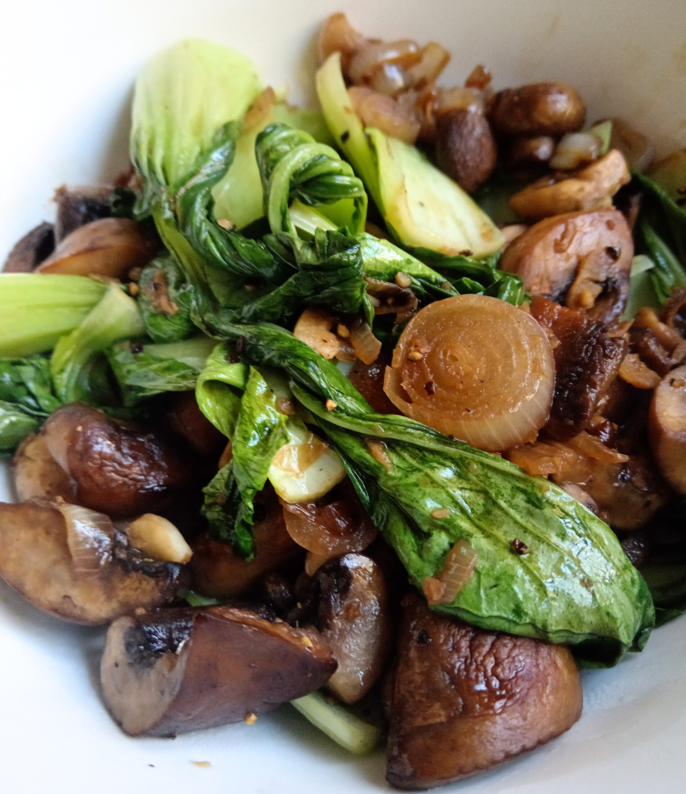 Butter-sautéed mushrooms, pak choi and shallots in a white serving bowl, finished with ginger, soy sauce, sesame oil and fresh lime.