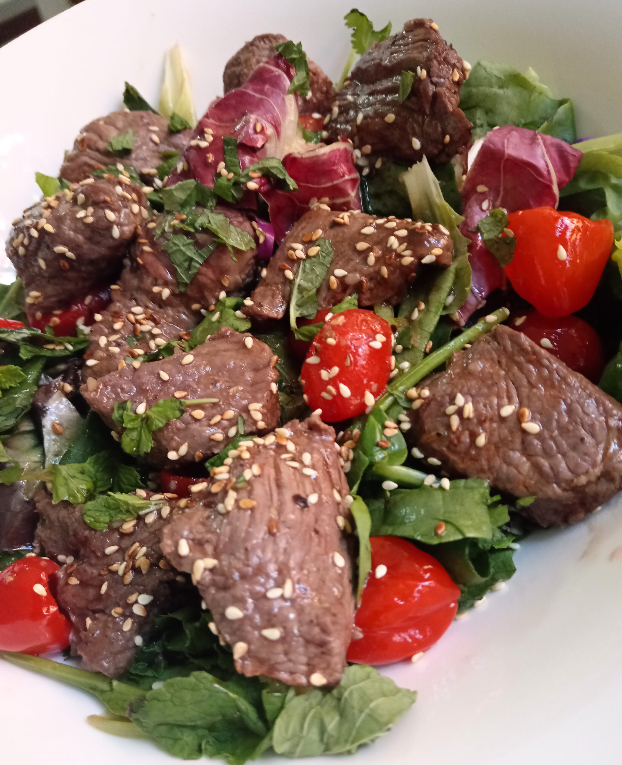 Bowl of mixed greens topped with seared ostrich cubes, peppadews, fresh mint, and toasted sesame seeds.