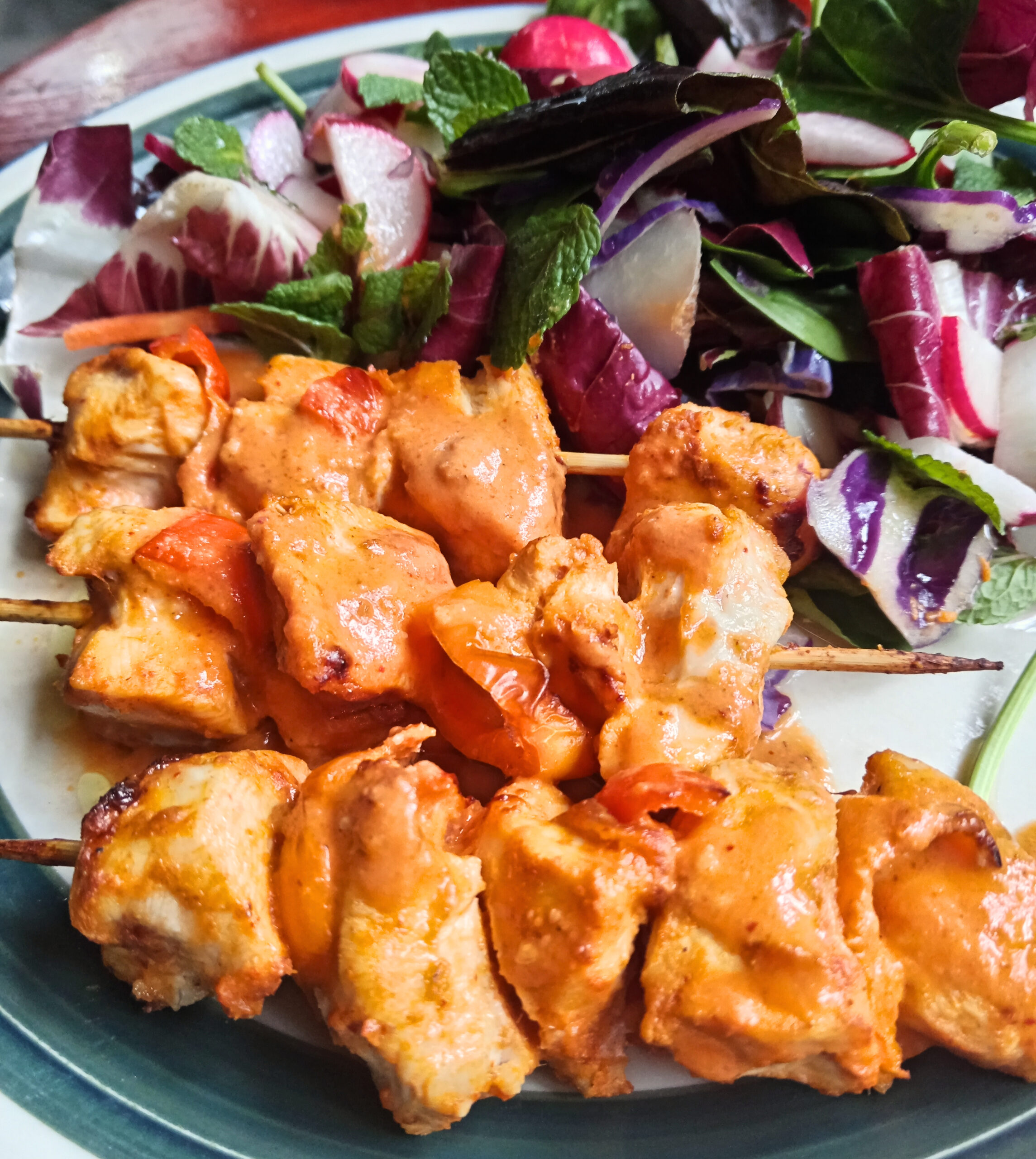 Thai Red Curry Chicken Skewers served with a fresh salad of mixed leaves, radishes, and mint.