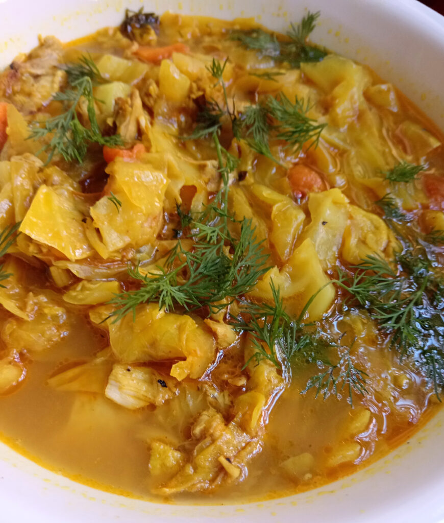 Bowl of turmeric lemon chicken soup with tender cabbage, shredded chicken, carrots, and fresh dill in a golden broth.